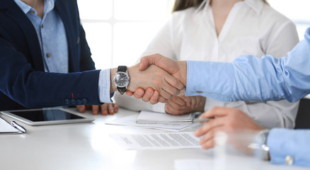 Business people shaking hands at meeting or negotiation, close-up. Group of unknown businessmen and women in modern office. Teamwork, partnership and handshake concept