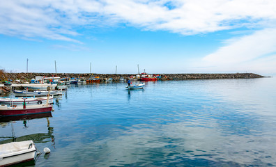 Obraz premium Colorful fishing boats in a harbour on a clear sunny day with blue skies reflected in the calm water.