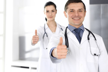 Fototapeta premium Group of doctors cheerful smiling at camera, thumbs up. Perfect medical service in clinic. Happy future in medicine and healthcare