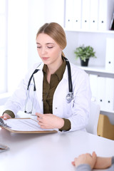 Young woman doctor and patient at medical examination in hospital office. Khaki colored blouse of therapist looks good. Medicine,  healthcare and doctor's appointment concept