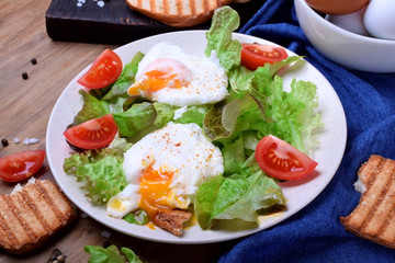 Poached egg with liquid yolk and green salad on a white plate