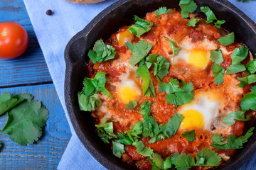Shakshuka with tomato sauce and quail eggs topped with cilantro in a cast iron pan. Jewish cuisine meal