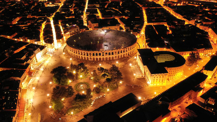 Aerial drone night shot from iconic illuminated Arena theatre and City Hall in Bra square of...