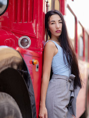 A beautiful young Asian woman stands and leans on a red bus in London while traveling in England