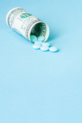 Money dollar rolled up with pills flowing out isolated on blue background, high costs of expensive medication concept. Copy space