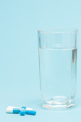Swallowing tablets. Pills and a glass of water against a blue table background. Top view, copy space, flat lay