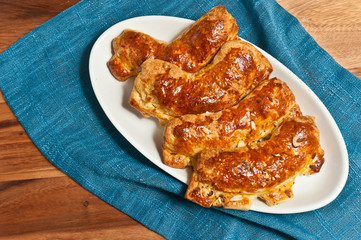 Top view, close distance of a freshly baked, homemade, ripped open coconut, almond, bear claw danishes on a white, oval dish with an artisan fork  on a blue place mat