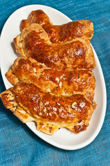 Top view, close distance of a freshly baked, homemade, ripped open coconut, almond, bear claw danishes on a white, oval dish  on a blue place mat