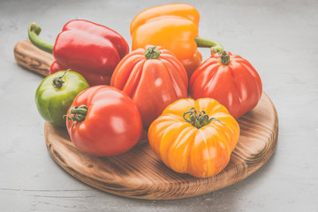 Selection of organic large heirloom tomatoes and peppers on the wood board, on grey concrete background, selective focus