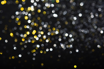 Abstract blurred glitter bokeh background in silver gold, on black
