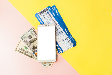 Smartphone, air ticket and dollars on pastel pink and yellow background. Minimal style, flatlay.