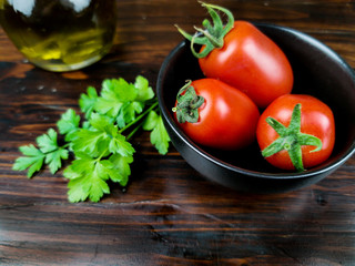 tomatoes in a black cup, olive oil and parsley on dark wood table 
