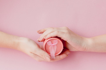 Round pink gift box in women's hands on a pink background. Festive concept for Valentine's day, Mother's day or birthday