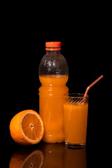 Bottle and glass with fresh orange juice and orange on a black background