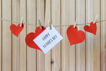 Fathers day concept. Message with paper hearts hanging with clothespins over light wooden board.