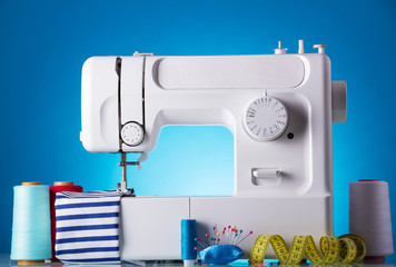 Modern white electric sewing machine with accessories for needlework on a blue