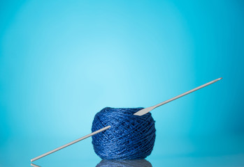 Skein of blue wool yarn for knitting and knitting needles on bright blue background