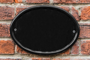 Blank black cast iron house number plate on a brick wall.