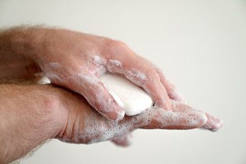 close up of man washing his hands with a bar of soap and soapy suds