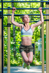 Fototapeta na wymiar muscular strong woman on the crossbar is engaged in the park, press exercises