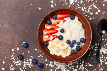 Bowl of oatmeal porridge with strawberry, blueberry and banana on table top view. Healthy breakfast.