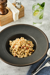 Barley porridge with chicken and bacon in a dark plate on a light table