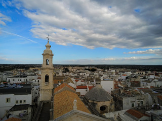 Fototapeta na wymiar Aerial Shot of the Belltower of the Church of the Nativity in the City of Noci, Near Bari, in the South of Italy, on Partially Cloudy Sky Background