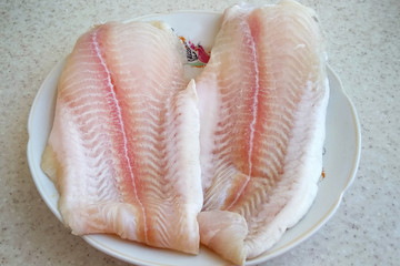 Two pieces of raw hake fillet on a plate. Cooking fish fillets at home.