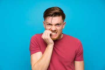 Redhead man on isolated blue wall nervous and scared