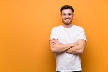Redhead man over brown wall keeping the arms crossed in frontal position