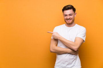 Redhead man over brown wall pointing finger to the side