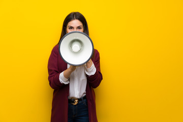Young woman over yellow wall shouting through a megaphone