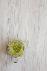 Green celery smoothie in a glass jar over white wooden surface, top view. Overhead, flat lay. Space for text.