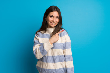 Fototapeta premium Young woman over blue wall pointing to the side to present a product