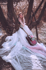 Fototapeta premium Beautiful romantic european girl with guitar with flowers inside, posing outdoors. Concept of music and nature. Spring time.