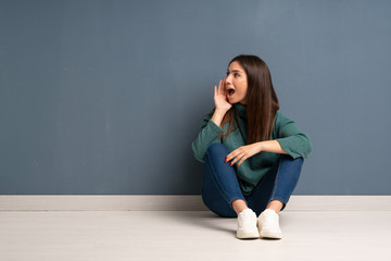 Young woman sitting on the floor shouting with mouth wide open to the lateral