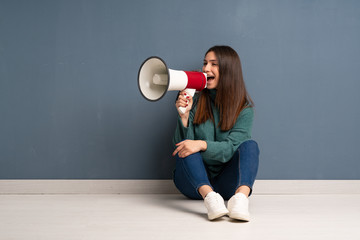 Young woman sitting on the floor shouting through a megaphone