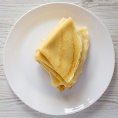 Pile of tasty blini on a white plate over white wooden surface, top view. Flat lay, overhead, from...