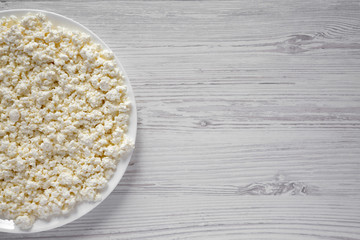 Homemade cottage cheese on a plate over white wooden background, top view. Copy space.