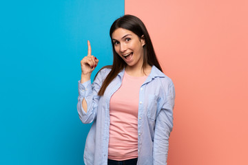 Fototapeta premium Young woman over pink and blue wall intending to realizes the solution while lifting a finger up
