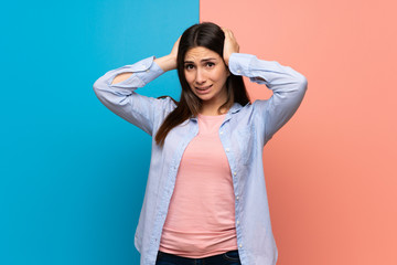 Young woman over pink and blue wall takes hands on head because has migraine