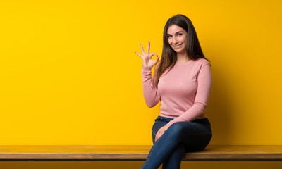 Young woman sitting on table showing ok sign with fingers