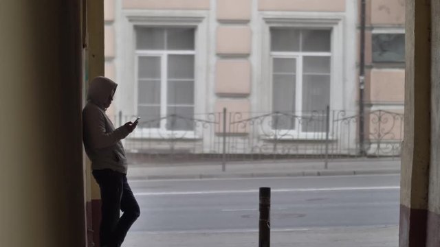 russian hooligan man stands in the arch on the street and uses the phone, waiting