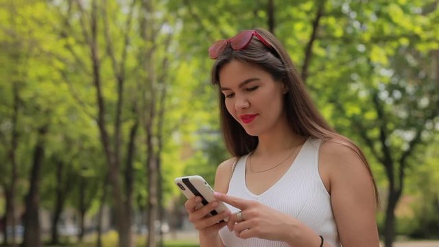 Woman reading message in smartphone chat walking at summer park