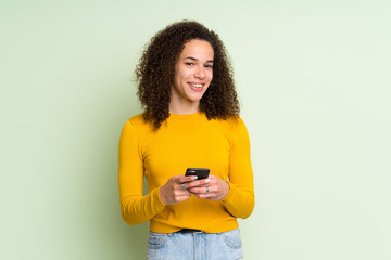 Dominican woman over isolated green background sending a message with the mobile