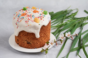 Easter composition Orthodox Easter cake decorated with white icing and multi-colored candied fruits on a gray background, egg, a branch of a blossoming tree