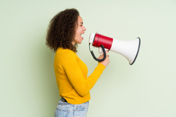 Dominican woman over isolated green background shouting through a megaphone