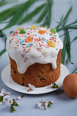 Easter composition Orthodox Easter cake decorated with white icing and multi-colored candied fruits on a gray background, egg, a branch of a blossoming tree
