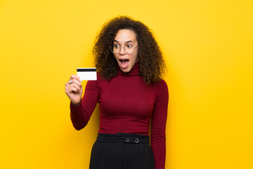 Dominican woman with turtleneck sweater holding a credit card and surprised