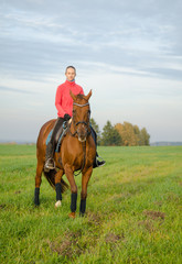 young woman riding horse in green meadow in autumn landscape